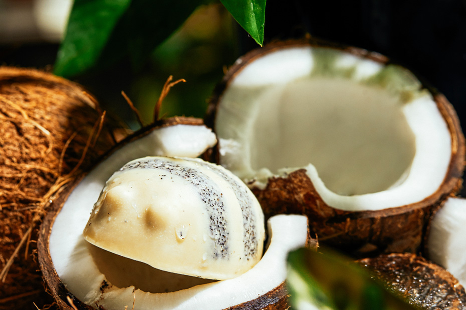 Scrubee Body Butter sits inside half a real coconut shell surrounded by other coconuts.