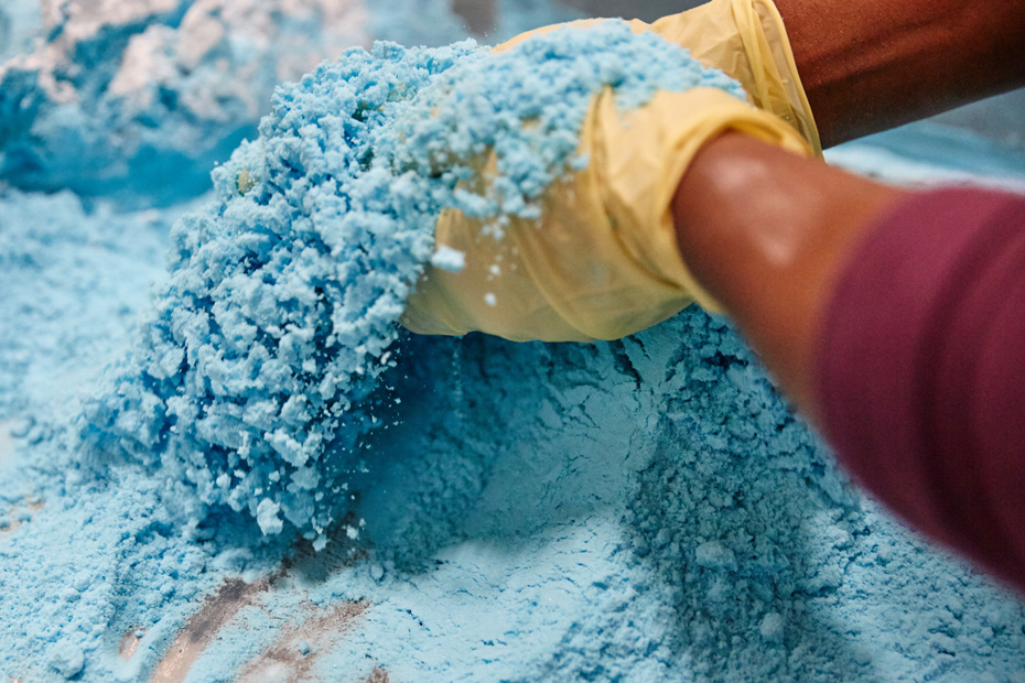 Gloved hands can be seen manipulating a blue powdery mix.