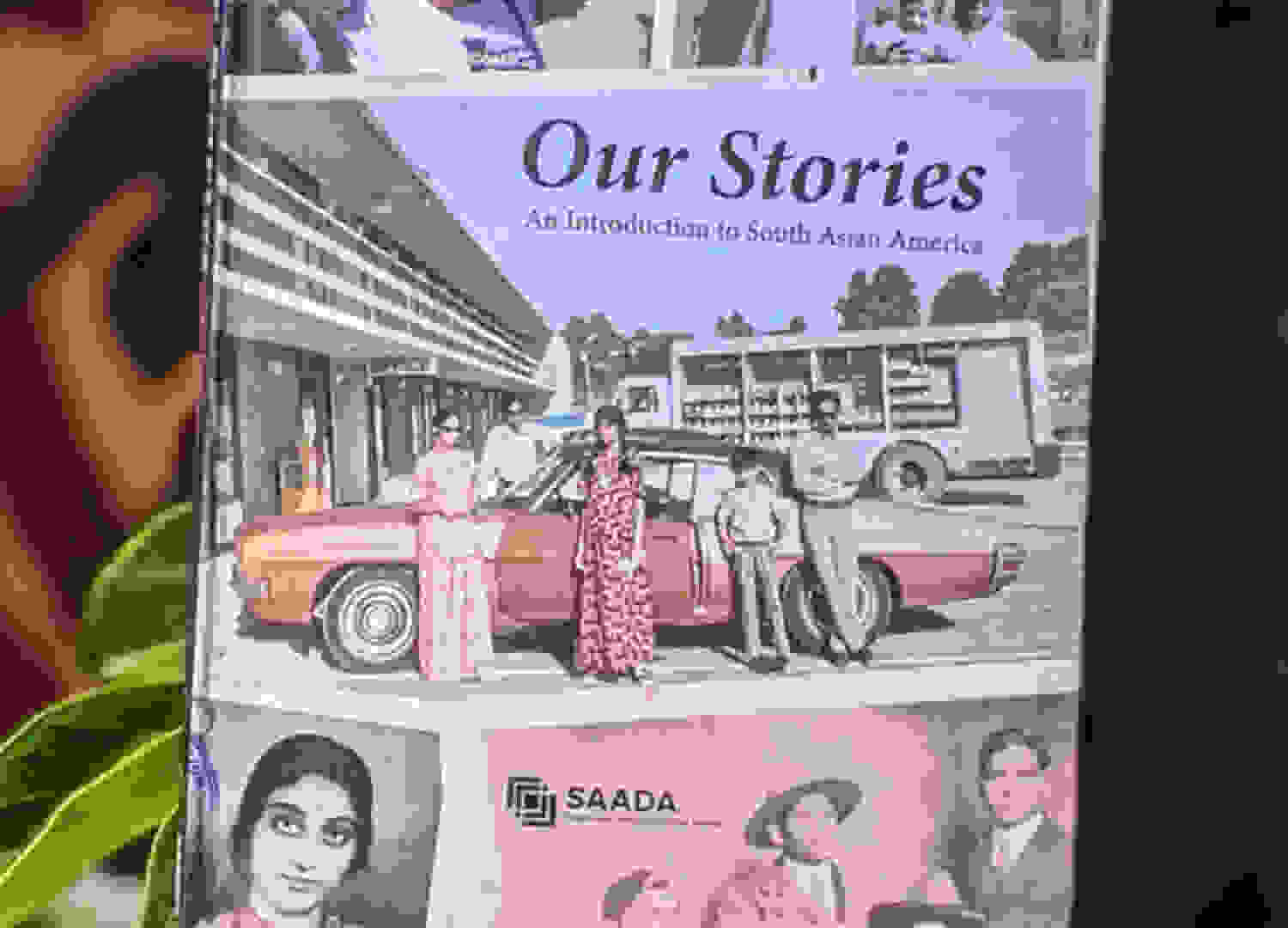 A hand holds up the book Our Stories: An Introduction to South Asian America