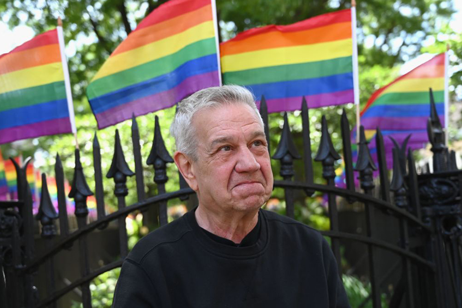 Activist Martin Boyce stands in front of four Pride flags.